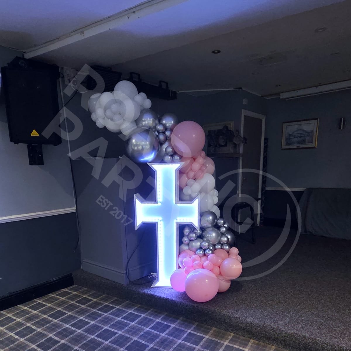 4ft Light Up Cross with Deluxe Balloon Garland around it in baby pink, silver and white at the MCA in Maghull
